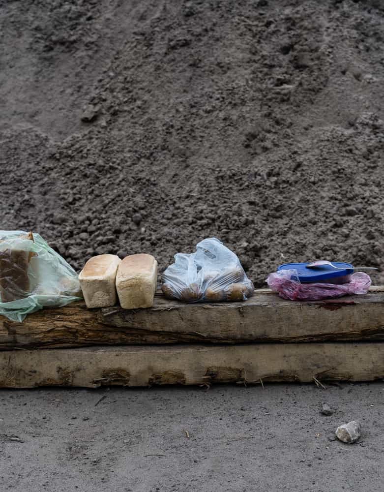 Два батона хлеба и другие продукты лежат на деревянном бревне на фоне кучи земли.